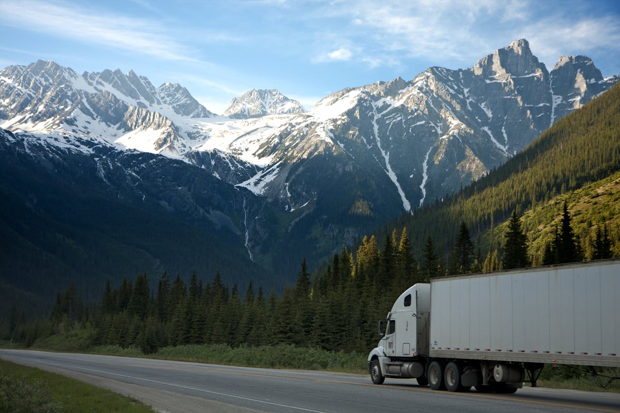pexels-photo-93398 A semi-truck travels along a highway with snow-capped mountains in the background.
