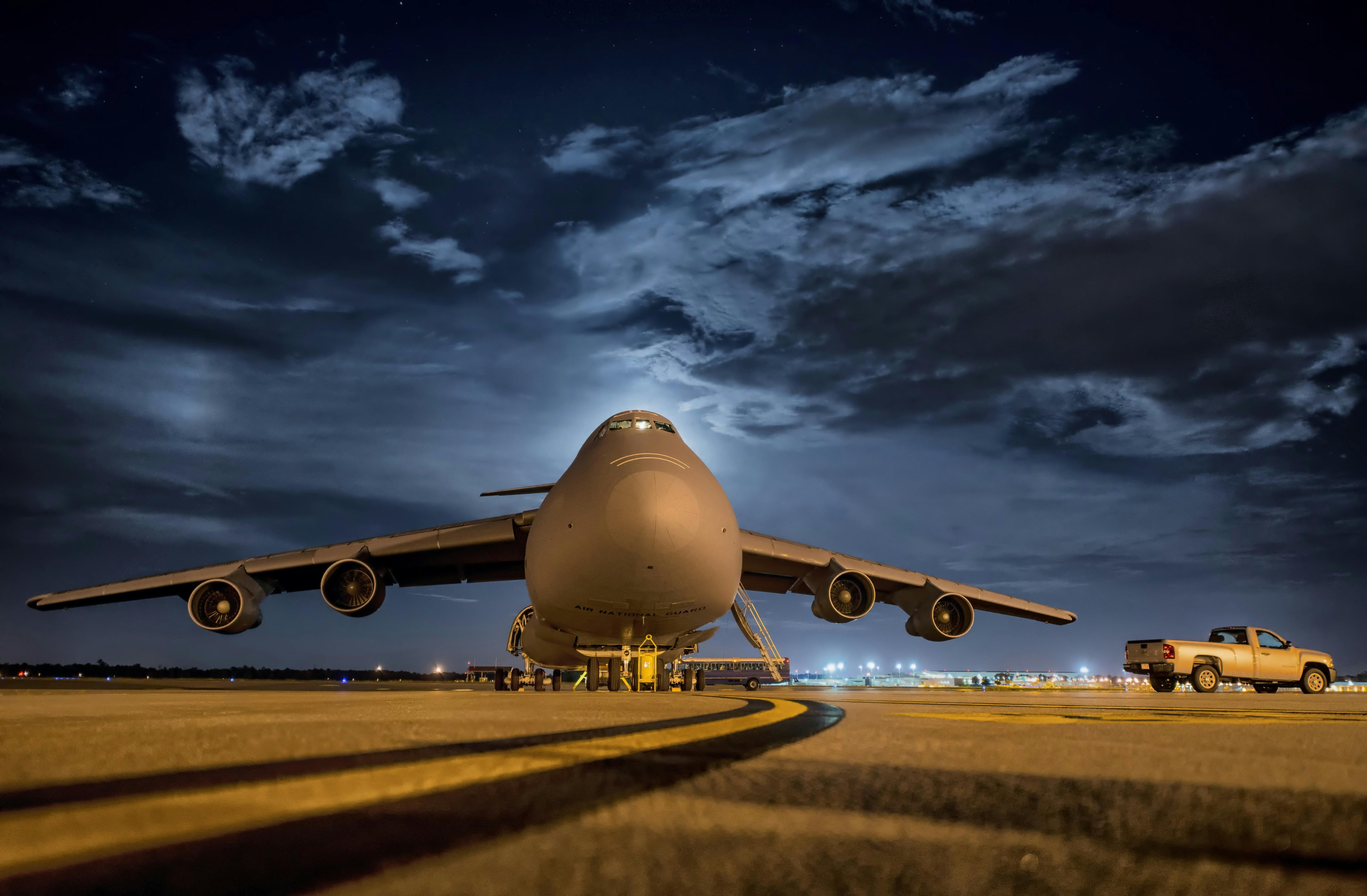 plane-aircraft-jet-airbase-67563-67563 A large cargo plane stationed on the tarmac under the night sky, ready for transport.